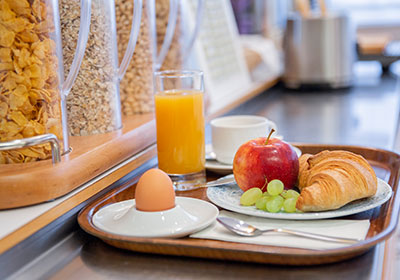 ein Frühstückstablett mit frischem Orangensaft, einem hart gekochten Ei, frischem Obst und einem Croissant