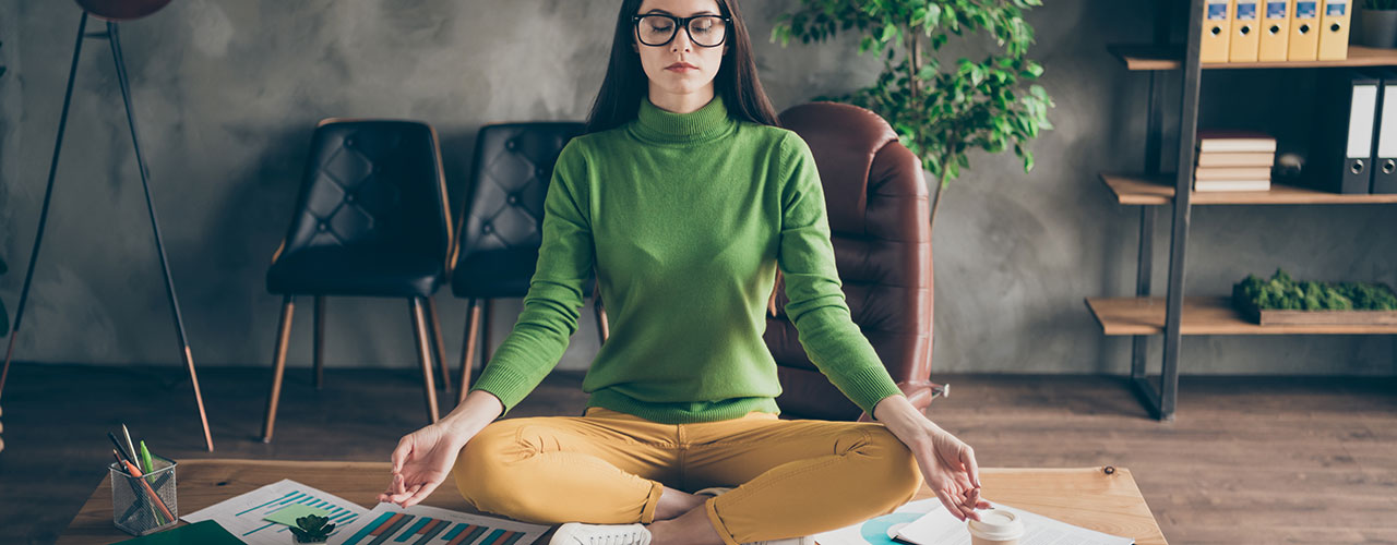 Frau in grünem Pullover macht Yoga auf ihrem vollem Bürotisch