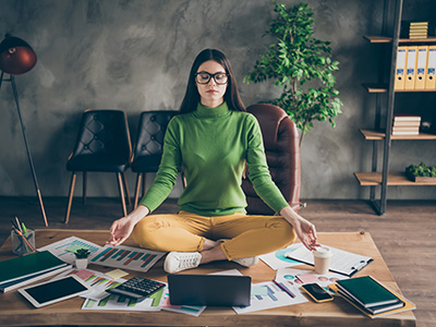 Frau in grünem Pullover macht Yoga auf ihrem vollem Bürotisch
